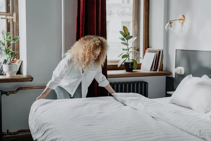 A housekeeper making up a bed in a short-let bedroom
