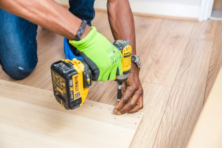 A tradesperson repairing a floor with a power drill